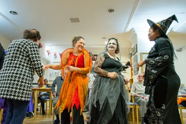 Team members dressed as witches dancing with a resident at the Halloween party.
